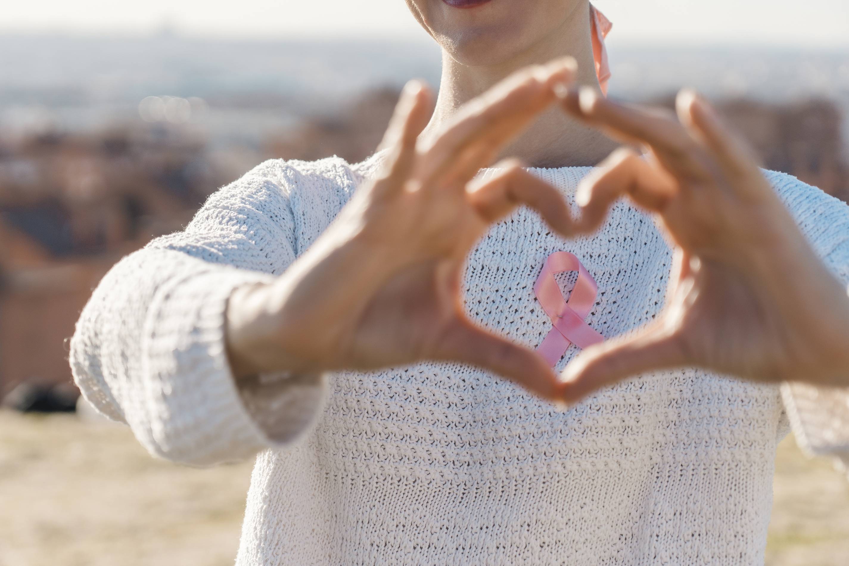 a woman makes a heart with her hands around a pink ribbon in support of breast cancer awareness