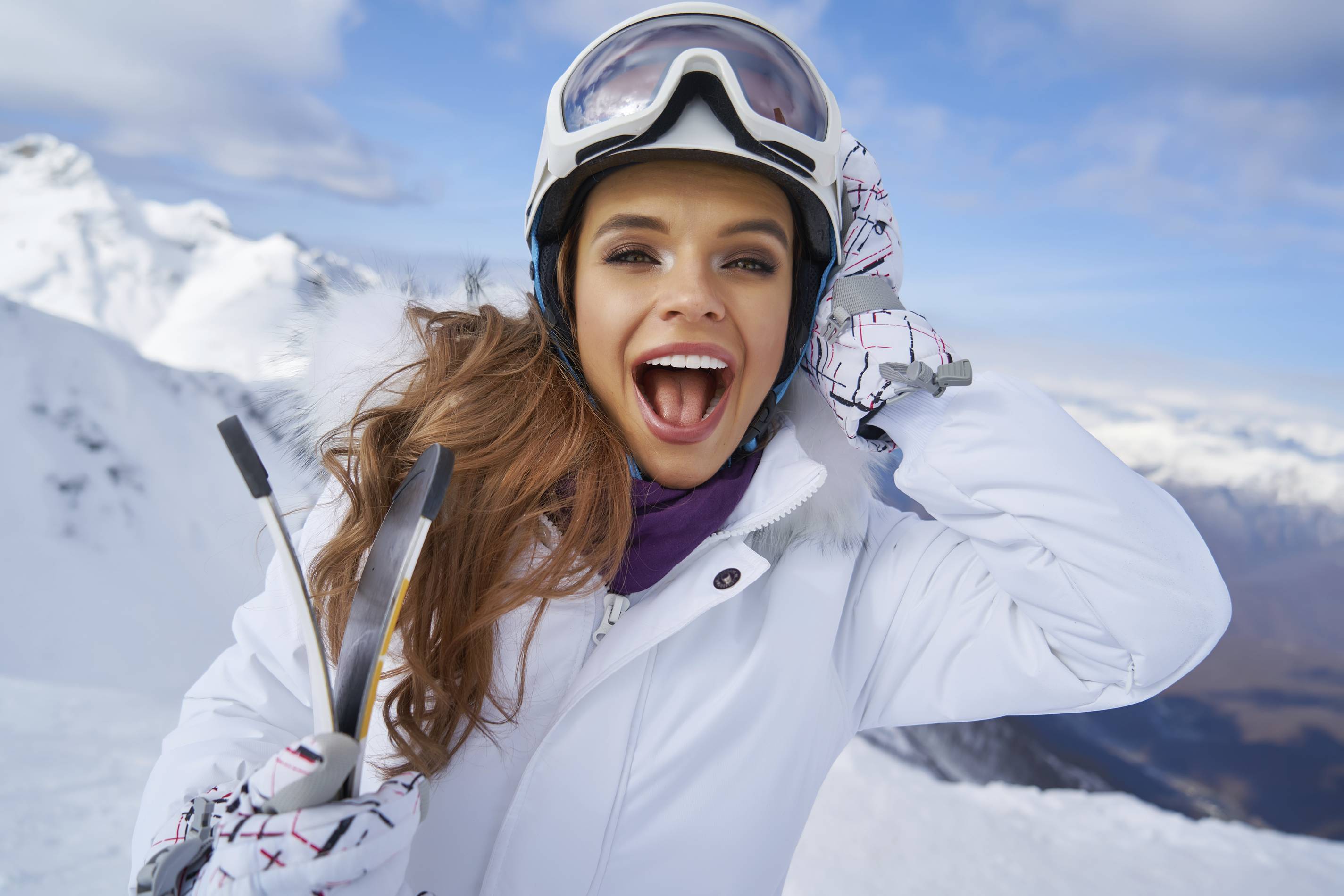 a woman smiles in a ski suit on the top of a mountain